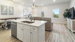 Una cocina moderna con una isla central, un comedor y una sala de estar con sofá y televisión.