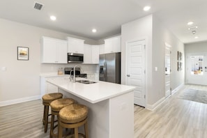 A modern kitchen with white cabinetry, stainless steel appliances, and a central island with stools.