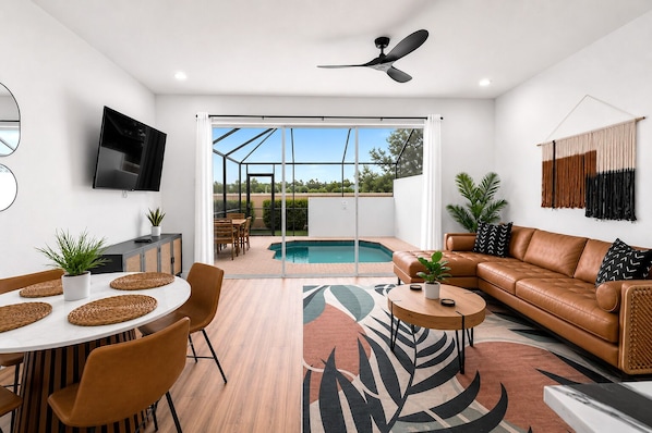 A modern living room with a pool, leather sofa, dining area, and a TV. - Windsor Hills Townhome - Theme Bedroom - Private Heated Pool - 2 Miles to Disney (Kissimmee)