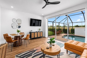 A modern living room with a dining area, a TV, and a poolside view. - Windsor Hills Townhome - Theme Bedroom - Private Heated Pool - 2 Miles to Disney (Kissimmee)