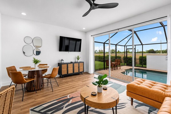 Uma sala de estar moderna com área de jantar, TV e vista para a piscina.