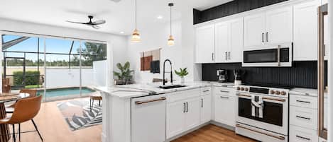 A modern kitchen with white cabinetry, a built-in oven, a microwave, and a dining area with a pool view.