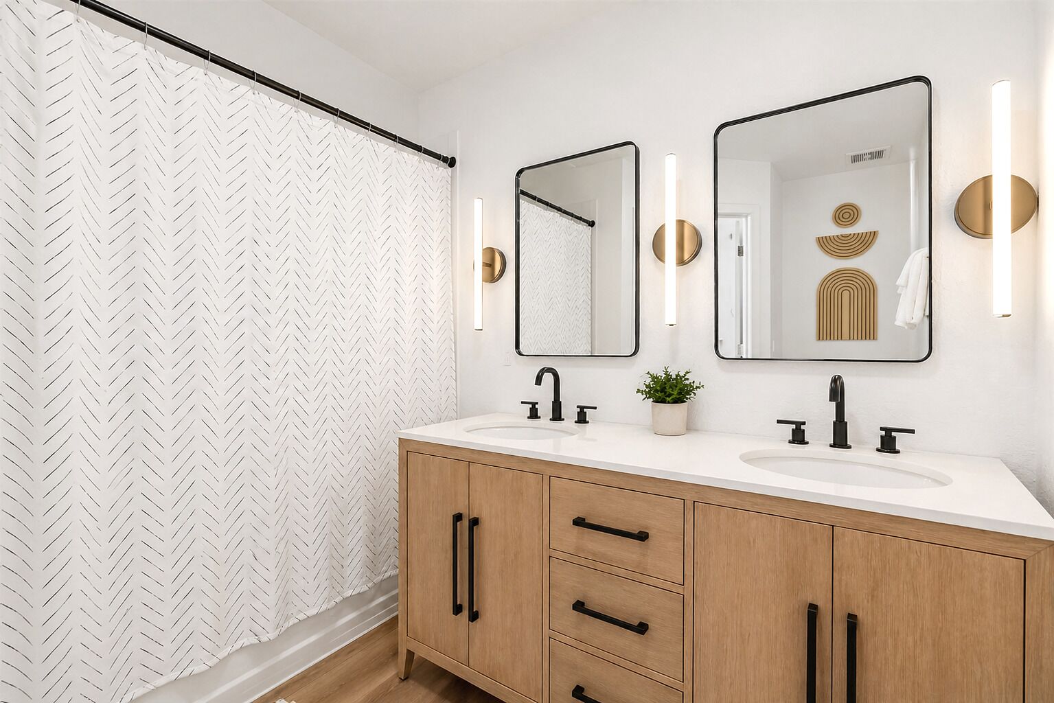 Une salle de bain moderne avec un rideau de douche à motif chevrons, un meuble-lavabo double et deux miroirs muraux agrémentés d’appliques.