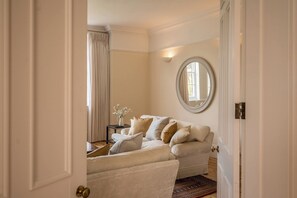 A room with a white sofa, a round mirror, a small table with a vase, and a patterned rug.