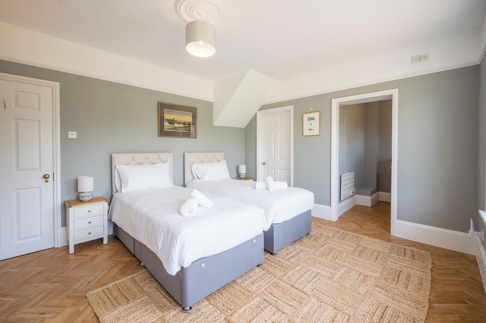 Een slaapkamer met twee bedden, een houten vloer, een groot tapijt en een plafondlamp.