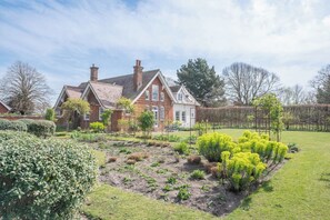 A large brick house with a well-maintained garden, including a vegetable patch and flowering plants.