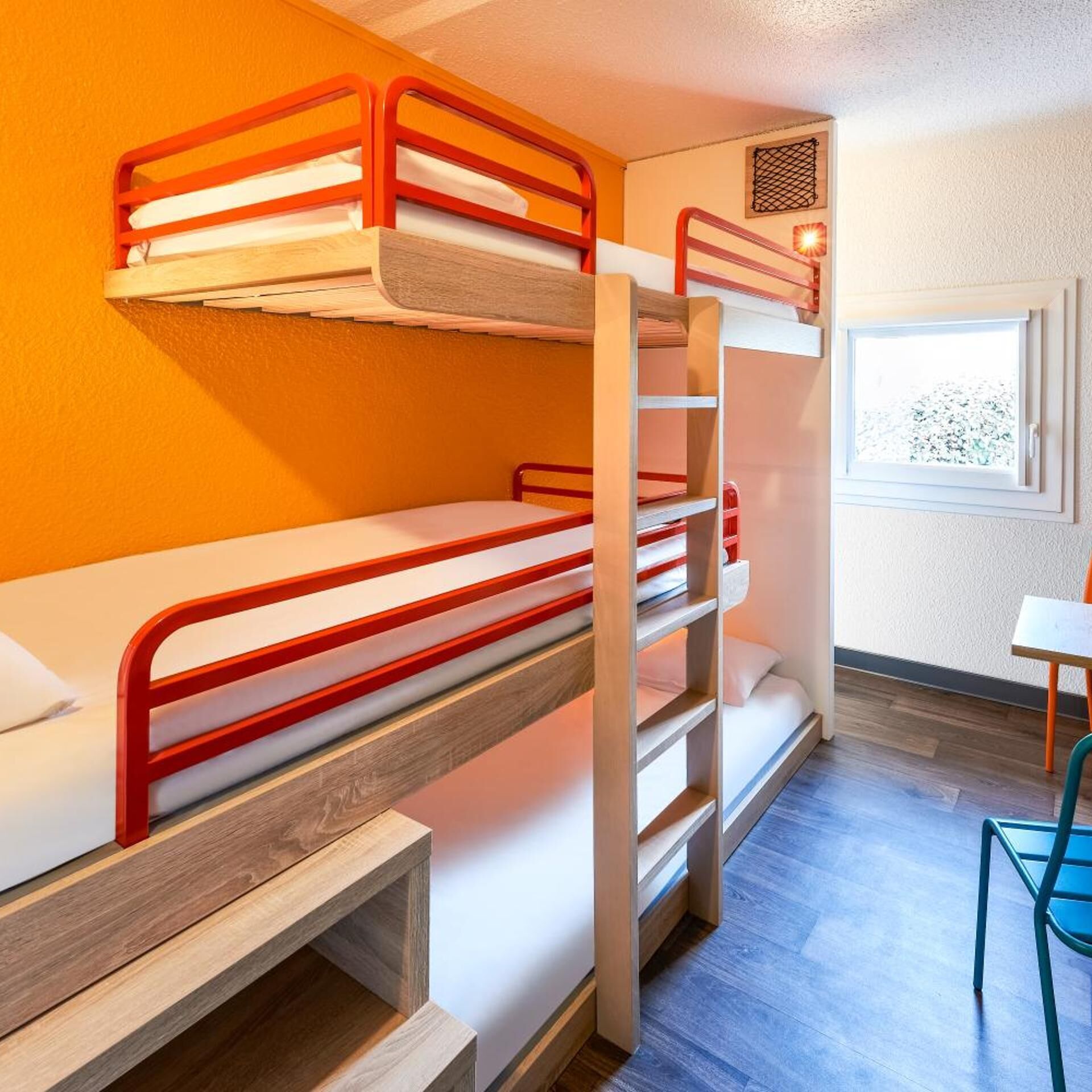 A bunk bed room with a wooden ladder, a small table, and a window with a view.