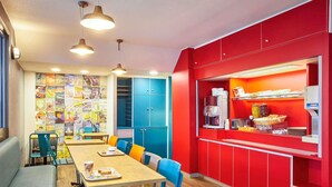 A dining area with a long table, blue chairs, and a red counter with a coffee machine. - Hotelf1 Marne la Vallee Collegien (Collegien)