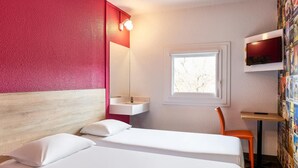 A hotel room with a bed, a small bedside table, a chair, a window, and a wall-mounted TV. - Hotelf1 Marne la Vallee Collegien (Collegien)