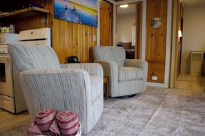 Una sala de estar con dos sillones, un sofá, una zona de cocina con microondas y un cuadro en la pared.