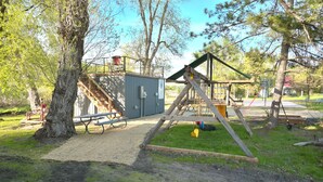 A playground with a swing set, picnic tables, and a covered area with a sign.