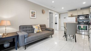A modern living room with a grey sofa, a small table with a lamp, and a kitchen area with a fridge, oven, and microwave. - Quiet 1BD in North Vancouver (North Vancouver)