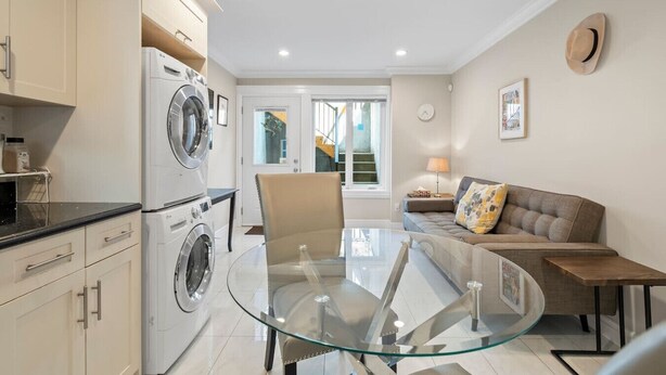 A modern kitchen with a washing machine, a glass dining table, and a sofa in a living area. - Quiet 1BD in North Vancouver (North Vancouver)