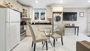 A modern kitchen with a glass dining table, two chairs, a refrigerator, a washing machine, and a TV. - Quiet 1BD in North Vancouver (North Vancouver)