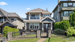 A two-story house with a front porch, a stone fence, and a well-maintained lawn. - Quiet 1BD in North Vancouver (North Vancouver)