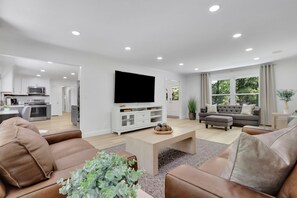 Una sala de estar moderna con un televisor de pantalla plana, sofás de cuero, una mesa de centro y una cocina al fondo.
