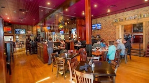 Un restaurant avec des tables et des chaises en bois, des murs en briques et un coin bar.