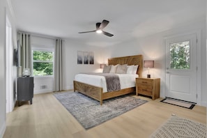Une chambre à coucher avec un lit, des tables de chevet, un ventilateur de plafond, une fenêtre avec des rideaux et une porte.