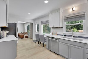 Una cocina moderna con armarios blancos, lavavajillas y un comedor con sofá y sillas.