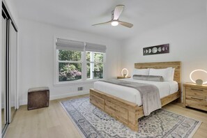 Un dormitorio con cama de madera, mesitas de noche, ventilador de techo, ventana con persianas y un cuadro de fases lunares colgado en la pared.