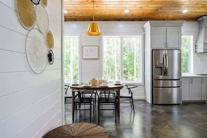 A modern kitchen with a stainless steel refrigerator, wooden ceiling, and a dining area with a round table and chairs. - NEW! Heated Pool, Hot Tub, Fire Pit, Outdoor Lounge - Sleeps 7 (Broken Bow)