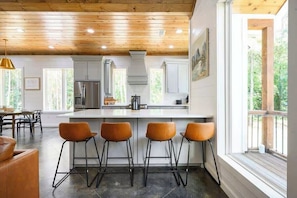 A modern kitchen with a central island, bar stools, and large windows. - NEW! Heated Pool, Hot Tub, Fire Pit, Outdoor Lounge - Sleeps 7 (Broken Bow)