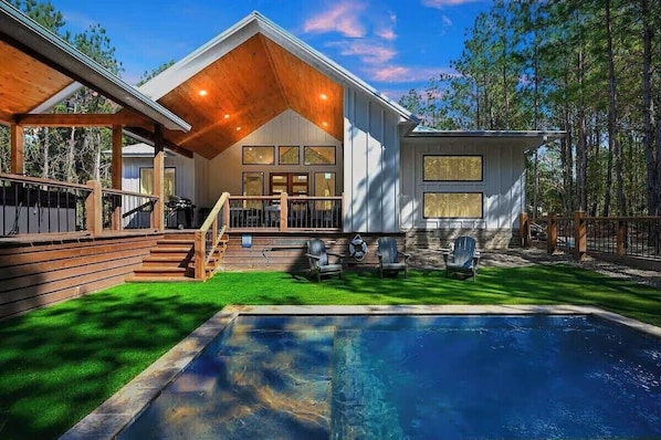 A modern house with a pool, wooden deck, and outdoor seating. - NEW! Heated Pool, Hot Tub, Fire Pit, Outdoor Lounge - Sleeps 7 (Broken Bow)