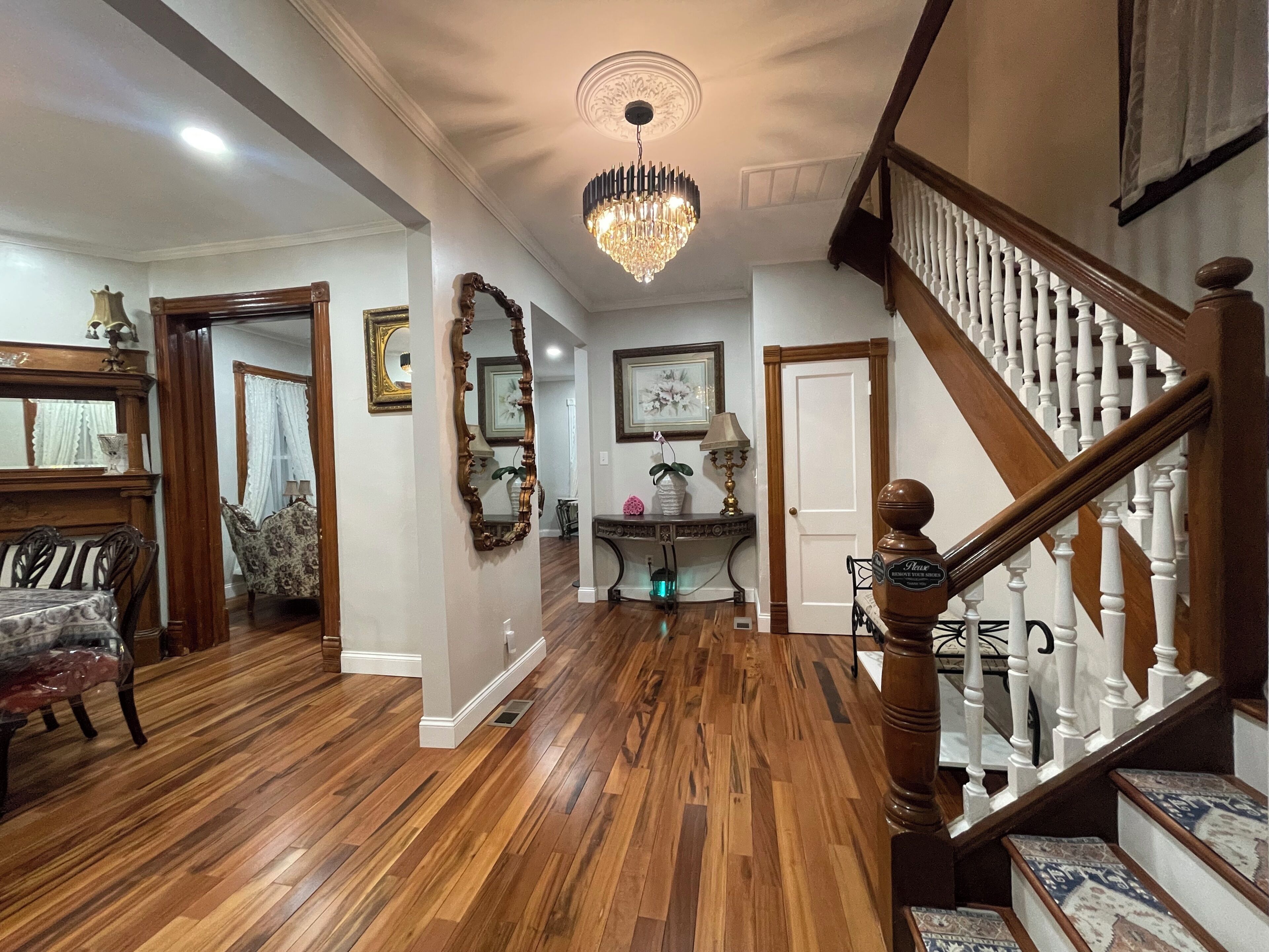 A spacious foyer with a wooden staircase, a chandelier, and a dining area with a table and chairs.