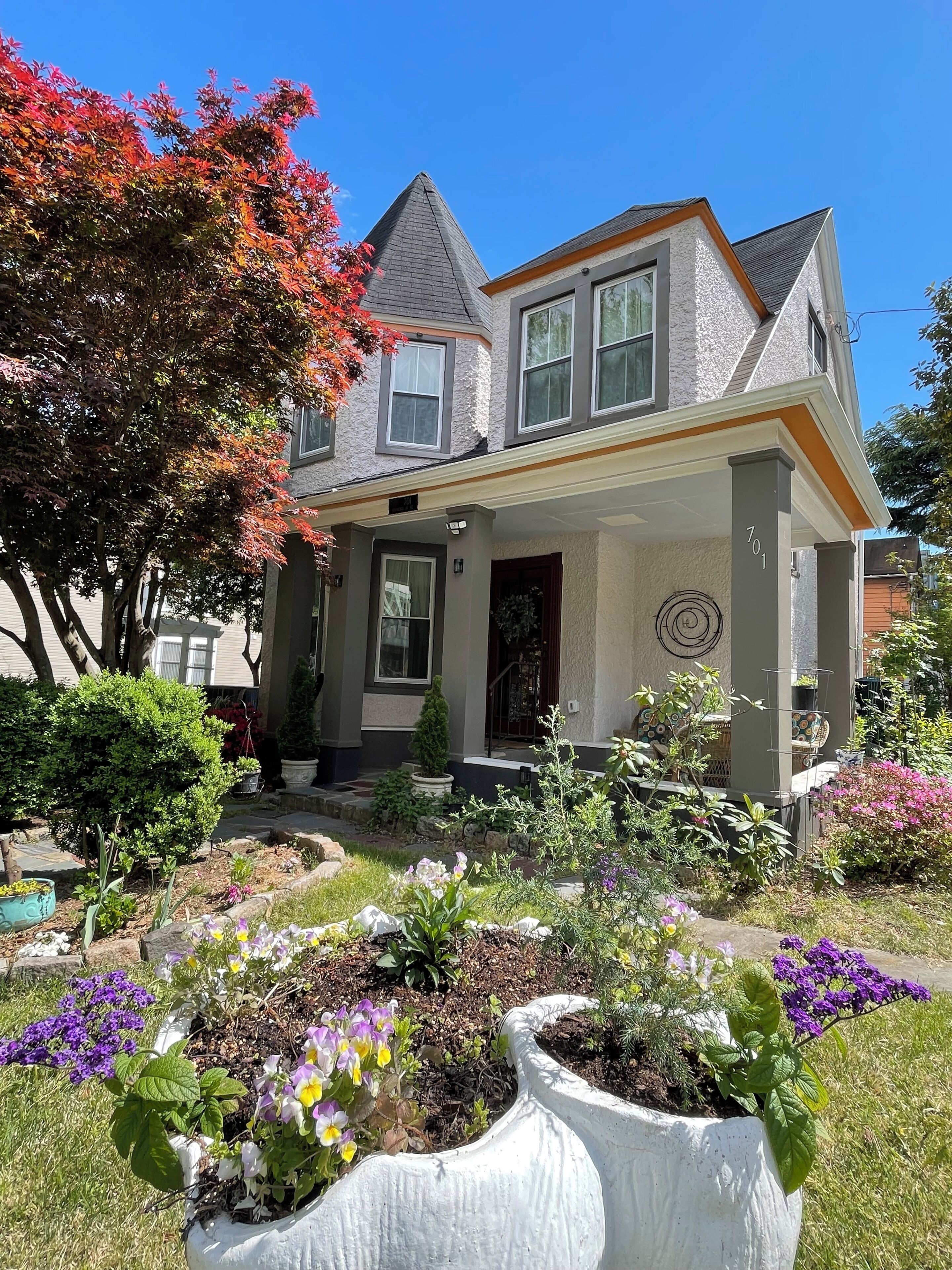 A two-story house with a gabled roof, a front porch, and a well-maintained garden with various plants and flowers.