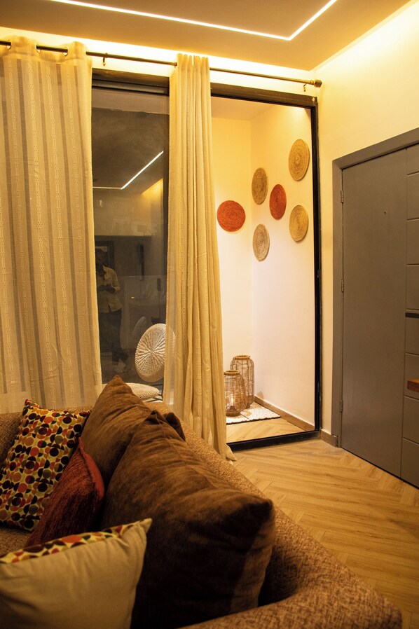 Una habitación con puerta de vidrio corrediza, un sofá con cojines estampados y una pared decorada con arte circular.