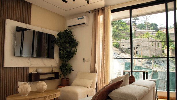 Un hotel moderno con sofá, televisor, planta en maceta y vistas al exterior.