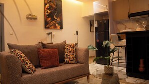 Una sala de estar con un sofá, una mesa de centro, una planta y una cocina con armarios y un refrigerador.