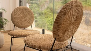 Un balcón con dos sillones de mimbre y una planta grande en maceta.