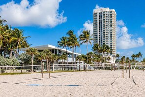Una playa con una red de voleibol, palmeras y un alto edificio de hotel.