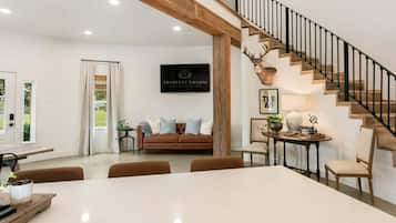Un vaste espace de vie doté d’un haut plafond, d’un escalier au revêtement en bois, d’une tête de cerf fixée au mur et d’une enseigne encadrée portant l’inscription « ABSOLUTE CHARM LUXURY ACCOMMODATIONS ».