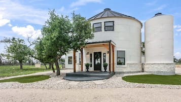Une maison à deux étages dotée d’un porche, de grandes fenêtres et de deux silos cylindriques.