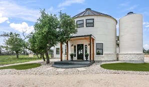 A two-story house with a porch, large windows, and two cylindrical silos. - Sileaux Ranch | Modern luxury farmhouse, minutes from Downtown (Fredericksburg)