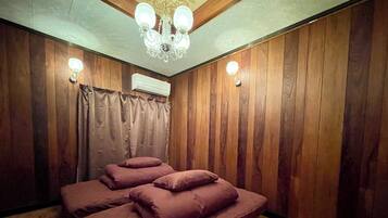 Una habitación con paneles de madera, una cama con muchos cojines, una araña y un equipo de aire acondicionado.