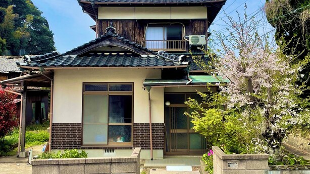 Una casa tradicional japonesa con tejado de tejas, fachada de madera y un pequeño porche.