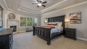 A bedroom with a large bed, a ceiling fan, a fireplace, and a window with a view. - Spacious retreat, pool and hot tub within walking distance of Lake Travis. (Spicewood)