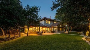 A house with a patio, a covered outdoor seating area, and a well-maintained lawn. - Spacious retreat, pool and hot tub within walking distance of Lake Travis. (Spicewood)