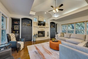 Ein geräumiges Wohnzimmer mit Kamin, Deckenventilator und großen Fenstern.