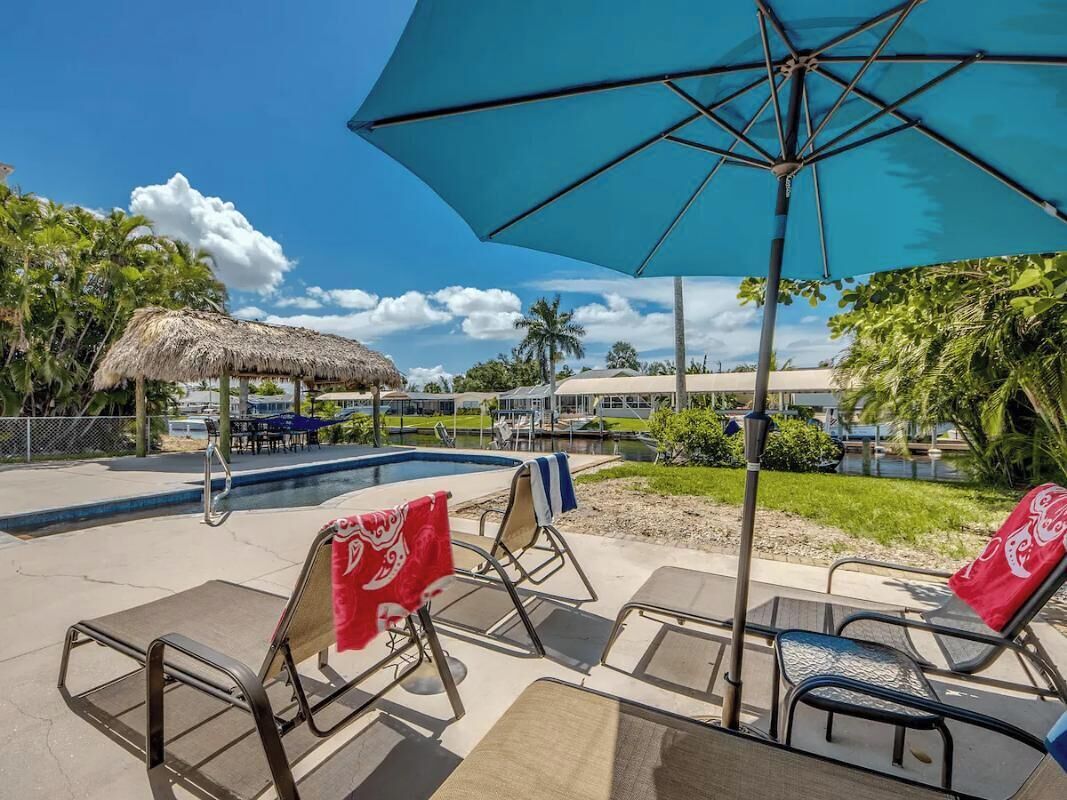 A pool area with lounge chairs, a thatched-roof structure, and a large umbrella.