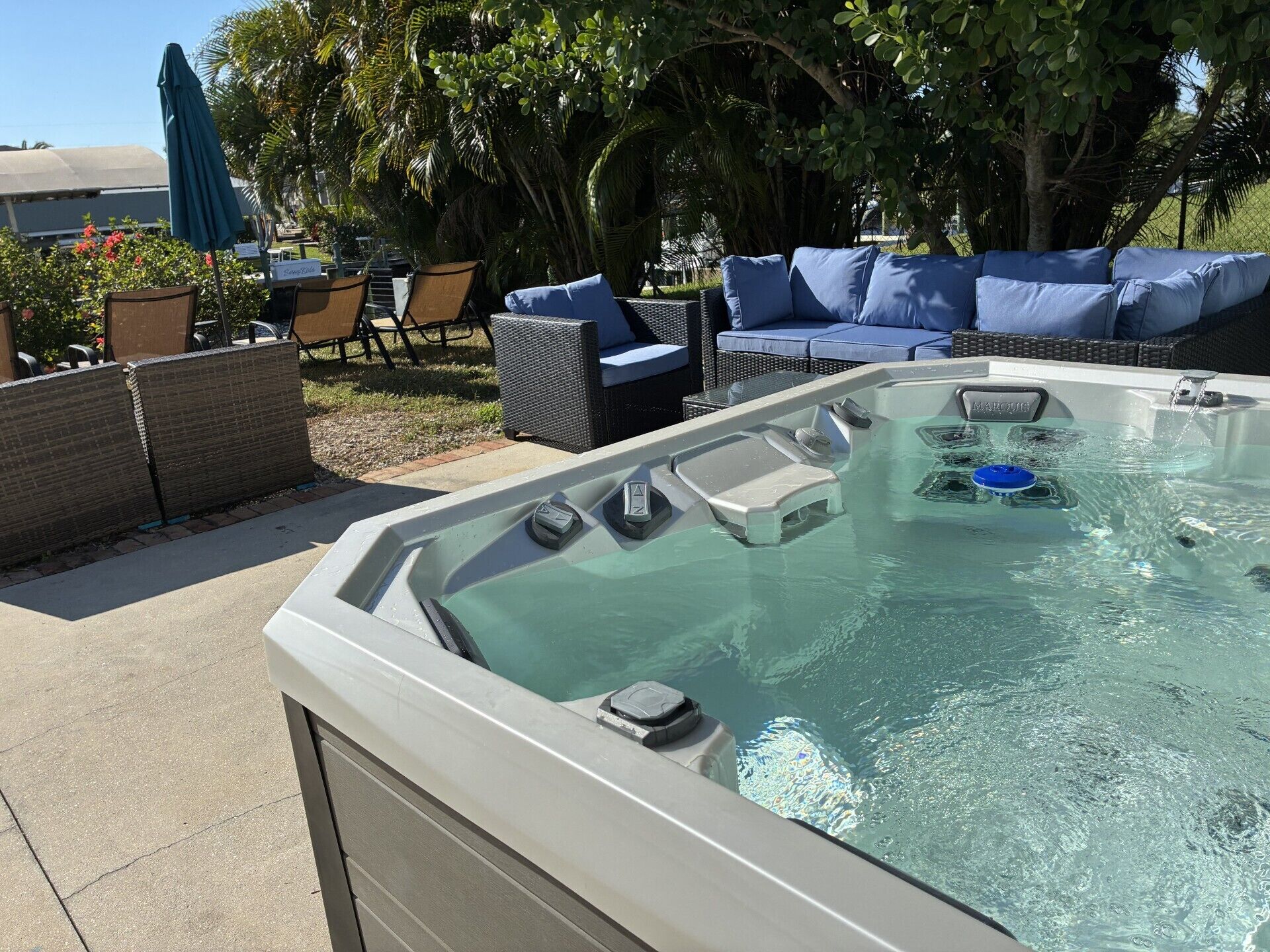 A hot tub with controls, surrounded by outdoor furniture and lush greenery.