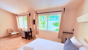 Quarto de hotel com cama, escrivaninha, cadeira e janela com cortinas.