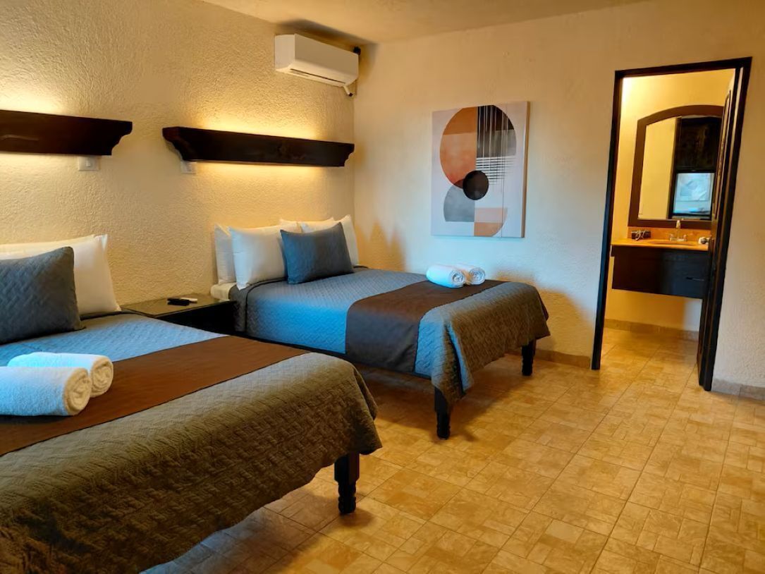 A hotel room with two beds, a nightstand, a mirror, and a wall-mounted artwork.