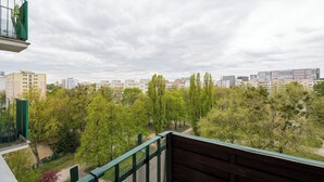 Ein Balkon mit Blick auf eine Stadtlandschaft, Bäume und einen bewölkten Himmel.