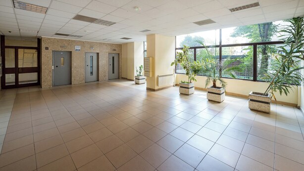 A spacious lobby with tiled floors, a reception desk, three doors, and potted plants. - Rondo ONZ Urban Core Apartment (Warszawa)