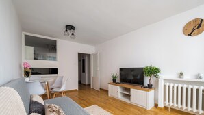 A modern living room with a sofa, TV, white cabinet, and a radiator. - Rondo ONZ Urban Core Apartment (Warszawa)