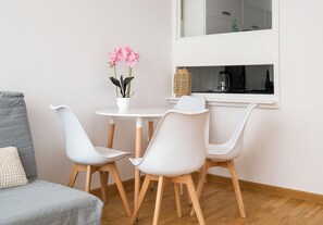Ein modernes Zimmer mit grauem Sofa, weißen Stühlen, einem kleinen Tisch mit Topfpflanze und einem Fenster mit Ausblick.